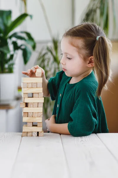 Cute little girl w zielonej sukience wprowadzenie drewnianego bloku na szczycie wieży Jenga — Zdjęcie stockowe