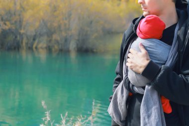 Çekici, genç bir baba ve bebeği açık havada asılıymış. İnsan çocuğunu taşıyor ve sonbahar dağ gölünde seyahat ediyor. Bebek giyme konsepti