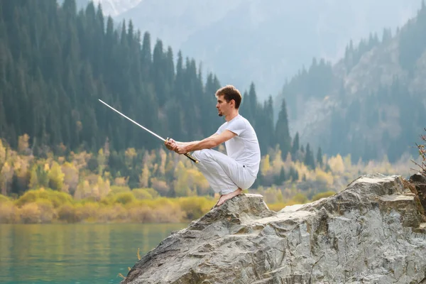 A barefoot man sits on a stone and holds a sword in his hands. Preparing for the battle. Man health concept