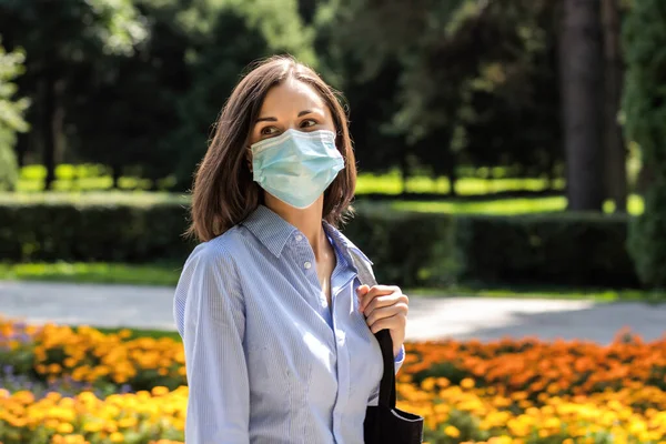 Mooie jonge vrouw wandelend in een zomerpark met een beschermend medisch masker — Stockfoto