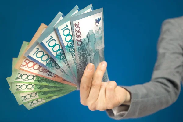 Primer plano de varias denominaciones de billetes de tenge de dinero kazajo en la mano sobre fondo azul. Enfoque selectivo —  Fotos de Stock