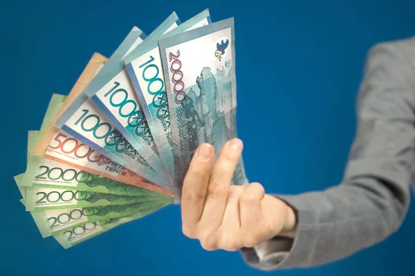Kazakistan 'ın çeşitli para birimlerinin yakın plan çekimleri mavi arka plandaki elde duruyor. Seçici odak