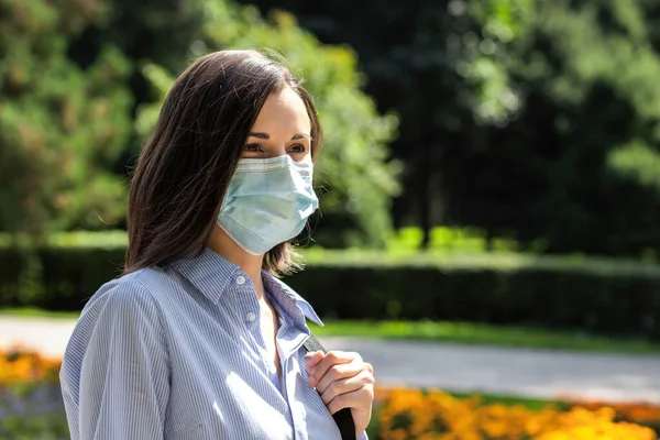 Schöne junge Frau Porträt in einem Sommerpark trägt eine schützende medizinische Gesichtsmaske — Stockfoto