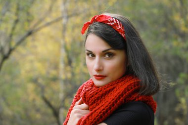 Beyaz önlüklü, tığ işi kırmızı atkı ve siyah şapkalı güzel bir kadın. Sonbahar açık havada gülümseyen portre.