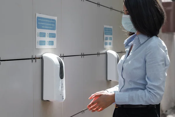 Young woman wearing a protective medical face mask and sanitizer on the outdoor wall in public place — Stock Photo, Image