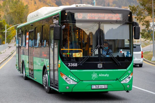 Yeşil şehir otobüsü Almaty caddesinde koruyucu maskeli bir şoförle sürüyor.