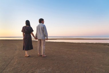 Akşam kumsalında yürüyen keten elbiseli genç aşıklar. Boşluğu kopyala