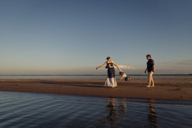 Genç ebeveynler deniz kenarında çocuklarıyla oynuyorlar.