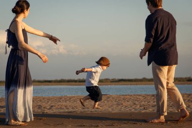 Kahverengi şapkalı küçük bir çocuk plaj boyunca anne ve babasından çok uzakta değil.