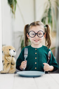 Yeşil muslin elbiseli küçük güzel kız kahvaltısını ayı oyuncağıyla bekliyor..