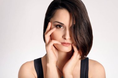 Güzel esmer kadın modelin portresi. Beyaz arka planda elleri yüzüne yakın.