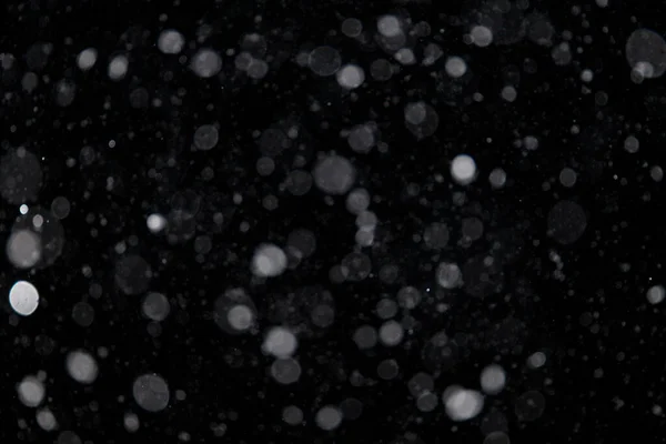 Falling snow out of focus on the black background. Snowfall for use as a texture layer in your project.