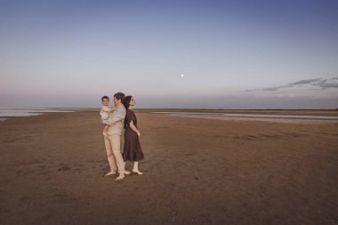 Genç ve güzel bir aile akşam kumsalında yürürken birlikte vakit geçirir. Boşluğu kopyala