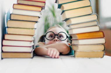Yuvarlak gözlüklü güzel, komik küçük kız okula hazırlanmak için bir sürü kitaba bakıyor. Temel eğitim konsepti.