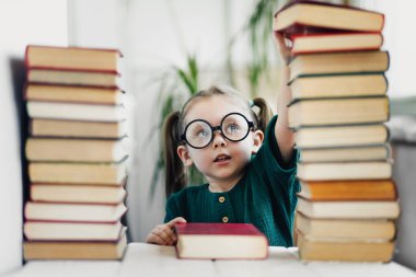 Kitap kulesinin tepesinden kitap alan güzel küçük bir kız. Okuma ve çocukların eğitim konsepti.