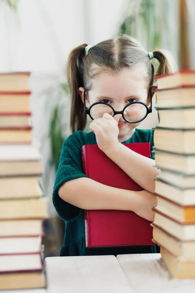 Cute little girl in green dress with red book in her hands fixing a glasses on her nose. Reading and education concept — Stock Photo, Image