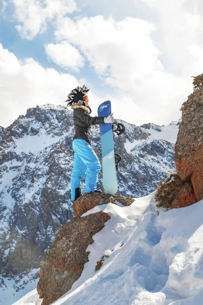 Freeride snowboarder mulher em chapéu mohawk no topo da rocha na montanha nevada. — Fotografia de Stock