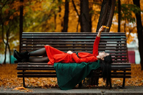 Ung Kvinna Orange Klänning Och Grön Rock Ligger Bänk Höstpark — Stockfoto