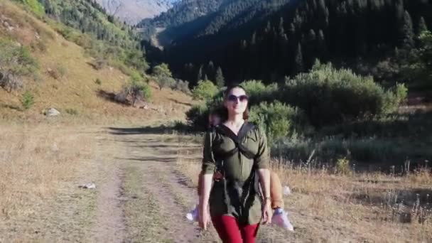 Молода жінка носить милу дитину в слінгу, проводячи вільний час на відкритому повітрі — стокове відео