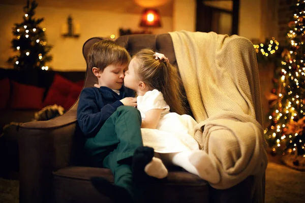 Little sister kisses his brother in a festive New Years interior with a Christmas tree — Stock Photo, Image