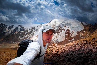 Trekker, Molodezhny buzulu ve Zailiyskiy Alatau ile Almaty yakınlarındaki arka planda selfie çekiyor..