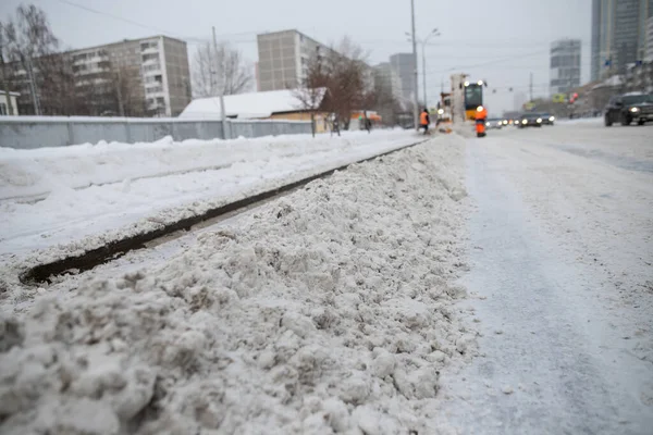 Tractor cleaning the road from the snow. Excavator cleans the streets of large amounts of snow in city. Workers sweep snow from road in winter, Cleaning road from snow storm.