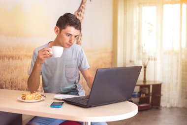 kahve yudumlarken bir dizüstü bilgisayar ve telefonu kullanan adam