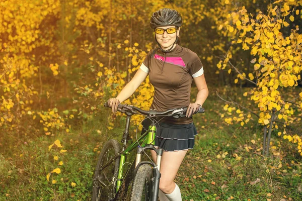 Woman biking in yellow autumn forest on a meadow