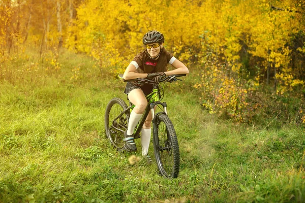 Woman biking in yellow autumn forest on a meadow