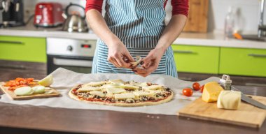 Önlüklü bir kadın şef çiğ pizzaya soğan halkaları koyuyor. Evde, mutfakta lezzetli pizzalar pişirmek..