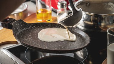 Bir insan hamuru sıcak tavaya döker ve lezzetli ev yapımı krepleri kızartır. Kendi mutfağında krep yapma kavramı..