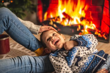 Anne ve küçük oğlu şöminenin yanında oturuyorlar, TV ekranında gösteriliyor ve eğleniyorlar. Evde rahat bir kış ortamı yaratma kavramı