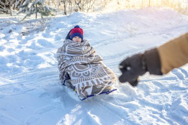Annem, soğuk bir kış gününde, açık havada kızakla gezen bir çocuğu çekiyor. Battaniyeye sarılmış bebek kızağa biniyor.