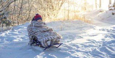 Annem, soğuk bir kış gününde, açık havada kızakla gezen bir çocuğu çekiyor. Battaniyeye sarılmış bebek kızağa biniyor.