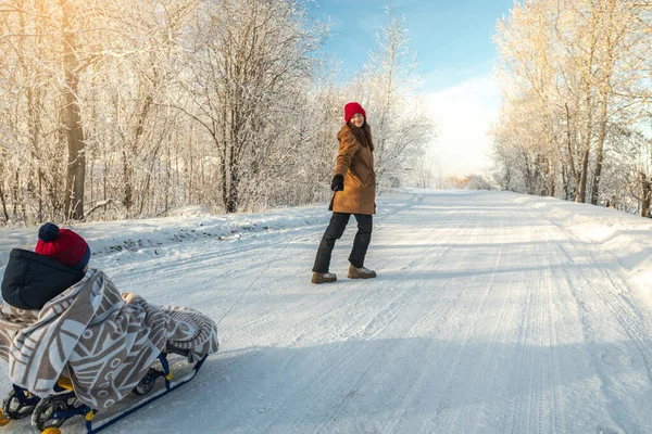 子供を持つ母親は晴れた日に霜の多い冬の朝を歩く そりに毛布に包まれた赤ちゃん — ストック写真