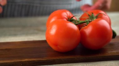 Şef iştah açıcı kırmızı domateslerden bir dal alıyor, bir domatesi koparıp, tahta kesme tahtasındaki keskin bir bıçakla ikiye bölüyor.