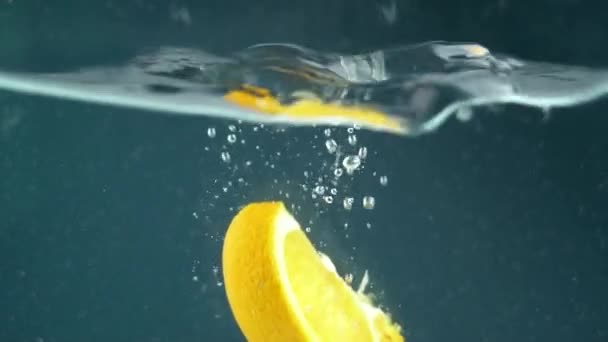 익은 오렌지 조각들이 맑은 물 속으로 떨어지면서 물보라를 일으키고 있다. 맛있고 즙이 많은 과일에 대한 개념 — 비디오