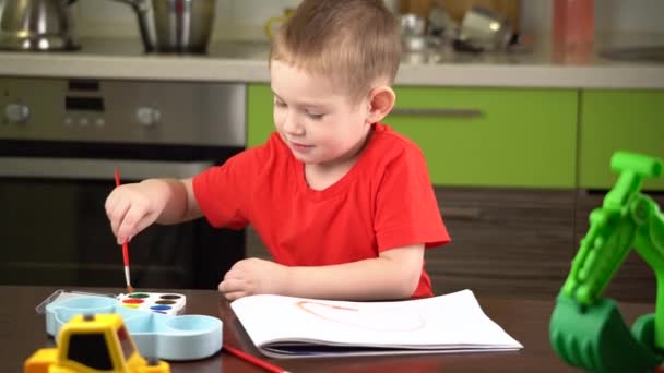 Kind in een rood T-shirt verft met kleurrijke aquarellen aan tafel — Stockvideo
