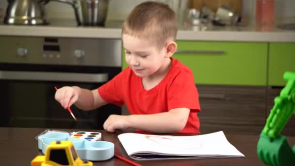 Niño en una camiseta roja pinta con acuarelas de colores en la mesa — Vídeos de Stock