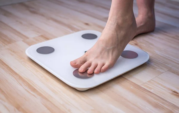 Women\'s bare feet stand on electronic scales on the wooden floor. The concept of fitness and weight loss tracking