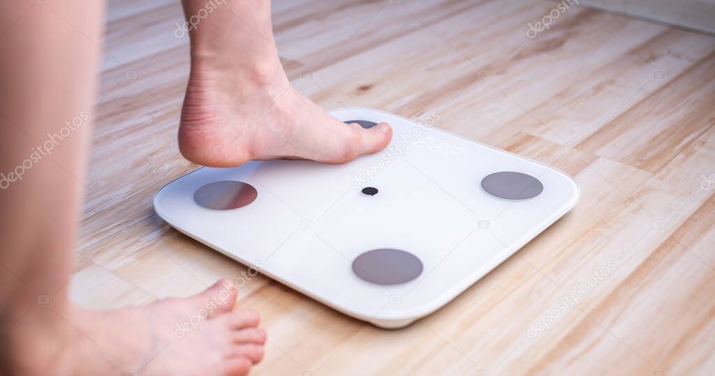 Women's bare feet stand on electronic scales on the wooden floor. The concept of fitness and weight loss tracking