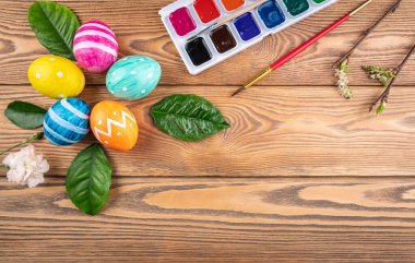 Ahşap arka planda yeşil yapraklar ve genç dallarla boyanmış el yapımı şirin Paskalya yumurtaları. Boşluğu kopyala