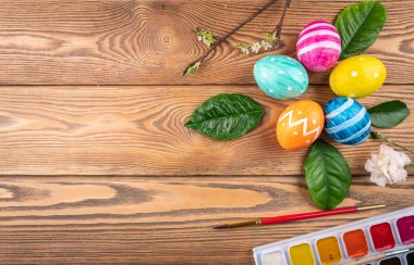 Ahşap arka planda yeşil yapraklar ve genç dallarla boyanmış el yapımı şirin Paskalya yumurtaları. Boşluğu kopyala