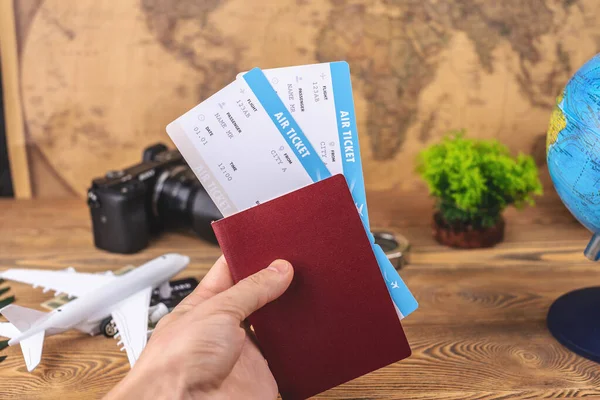 Hand is holding a passport and plane tickets over a wooden table with travel supplies. Vacation and booking concept. Top view.