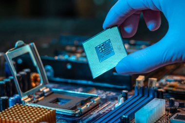 Mühendisin eldivenli eli CPU çipini ana kartın arka planında tutuyor. Yüksek teknoloji donanım mikro elektronik kavramı