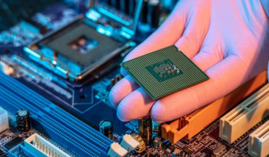 Mühendisin eldivenli eli CPU çipini ana kartın arka planında tutuyor. Yüksek teknoloji donanım mikro elektronik kavramı