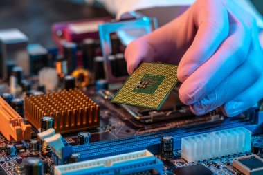 Mühendisin eldivenli eli CPU çipini ana kartın arka planında tutuyor. Yüksek teknoloji donanım mikro elektronik kavramı