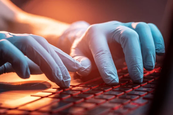 Hands in medical gloves type on a laptop keyboard in close-up. The concept of protection while working in quarantine