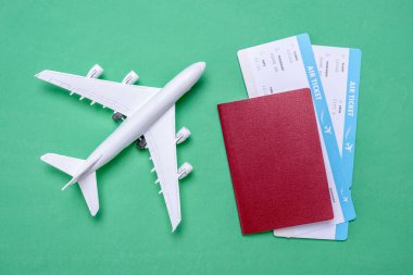 Uçağın minyatürü, uçak biletleri ve yeşil arka planda pasaport. Seyahat, tatil ve bilet rezervasyonu kavramı.
