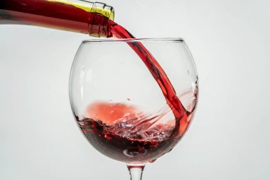 Kırmızı üzüm şarabı şişenin boynundan beyaz arka planda bir şarap bardağına dökülüyor. Tatma oturumu